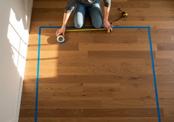 Person using tape on a bedroom floor to outline a bed.